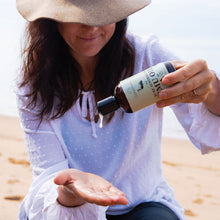 Load image into Gallery viewer, Middle aged lady pouring our 250m pure emu oil into he palm with beach in background
